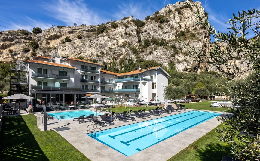 Hotel with outdoor pool and lounge chairs by rocky cliffs under blue sky