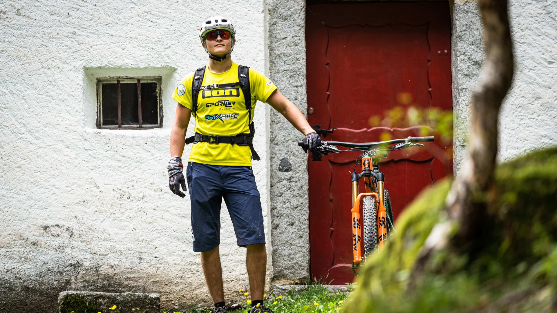 Mann mit Fahrradhelm und Fahrrad vor roter Tür an weißem Haus