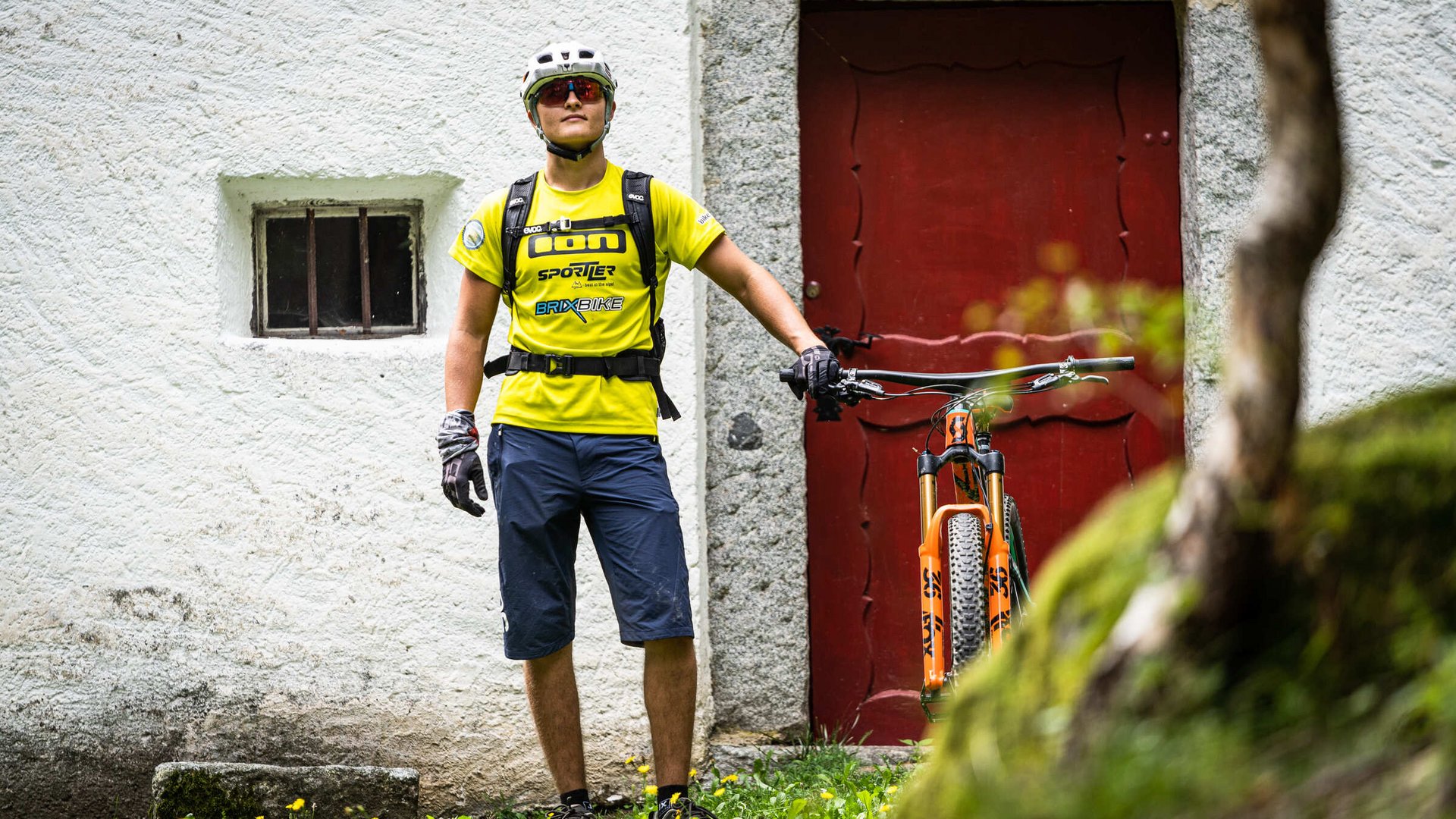 Mann mit Fahrradhelm und Fahrrad vor roter Tür an weißem Haus
