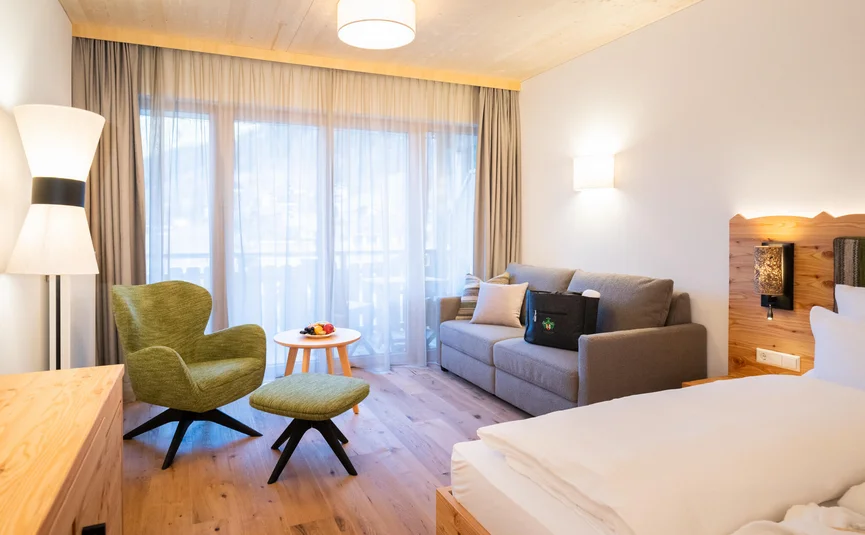 Gemütliches Hotelzimmer mit grünem Sessel, Sofa und großem Fenster
