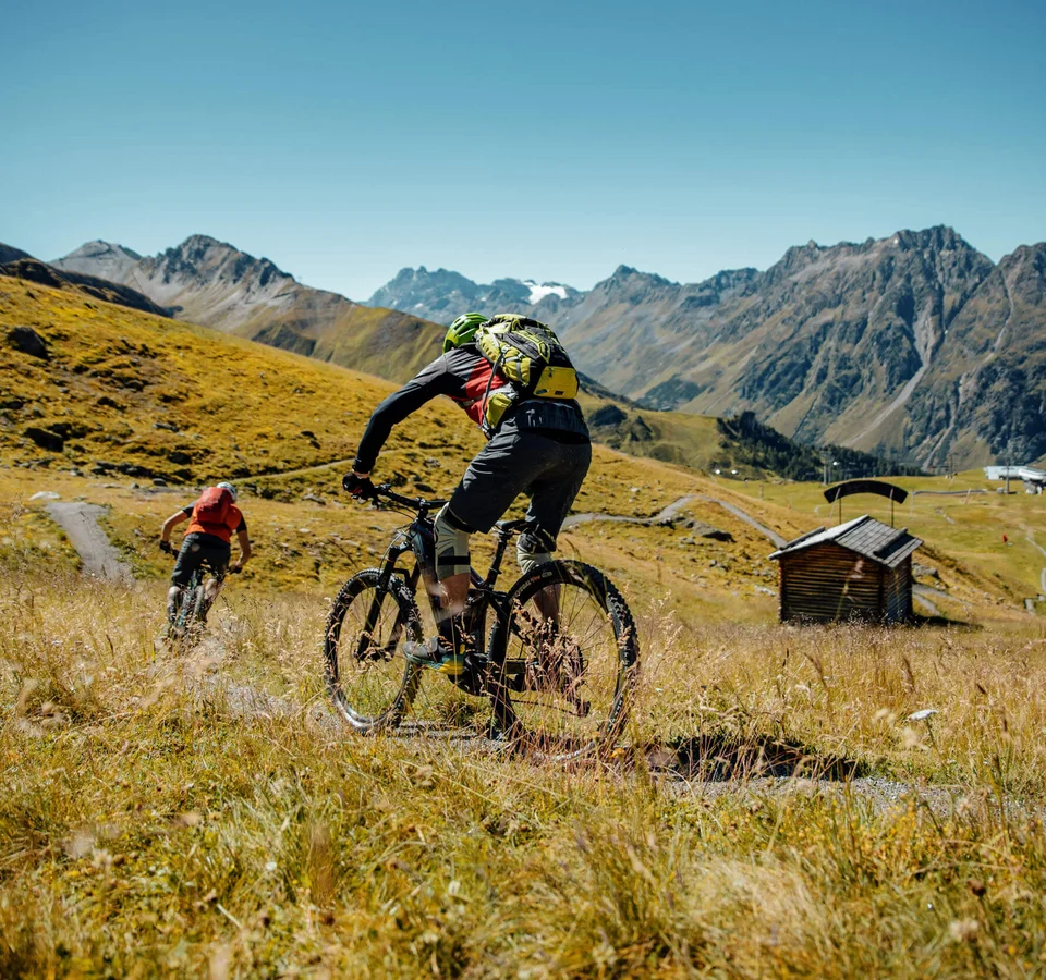 Zwei Mountainbiker fahren auf einem Pfad in den Bergen bei klarem Himmel