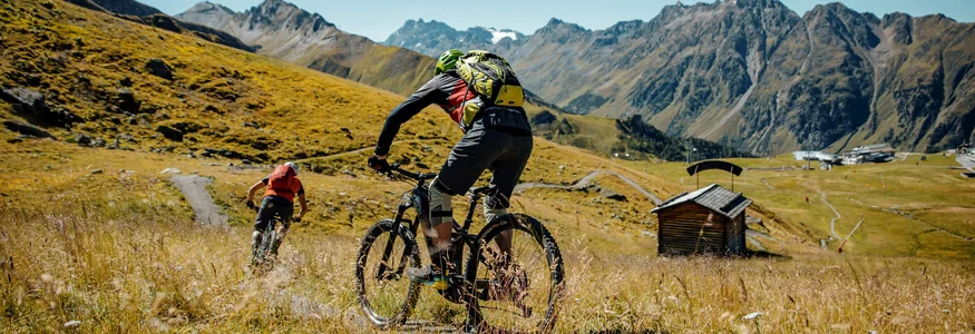 Zwei Mountainbiker fahren auf einem Pfad in den Bergen bei klarem Himmel