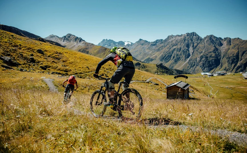 Zwei Mountainbiker fahren auf einem Pfad in den Bergen bei klarem Himmel