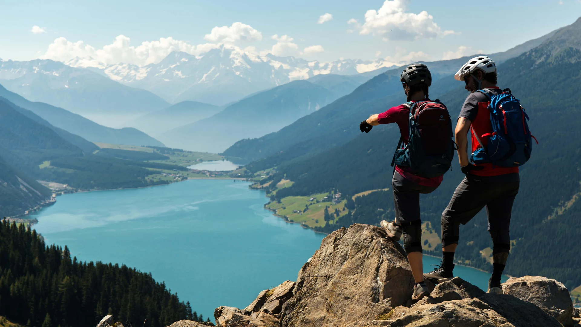 Zwei Wanderer mit Rucksäcken auf Felsen über blauem Bergsee