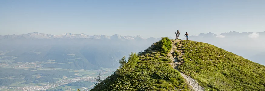 Zwei Radfahrer auf einem bergigen Wanderweg mit Tal- und Bergsicht