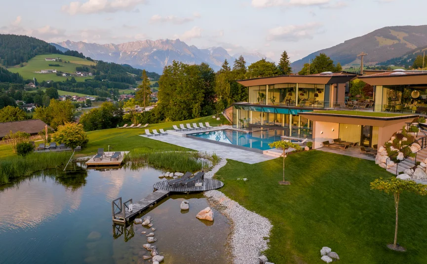 Modernes Hotel mit Pool und Teich in den Bergen bei Sonnenuntergang