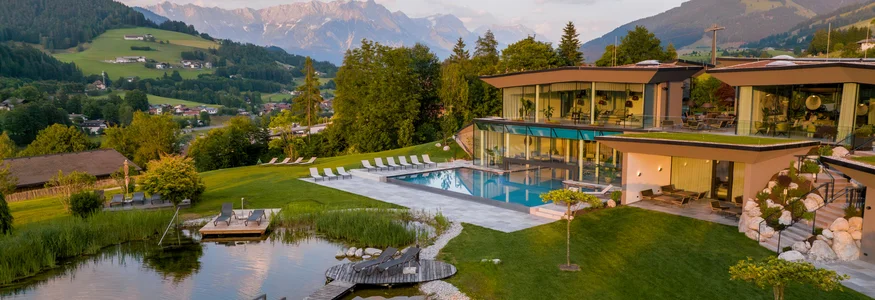 Modernes Hotel mit Pool und Teich in den Bergen bei Sonnenuntergang