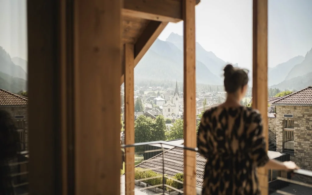 Woman looks out window at town with mountains in the background