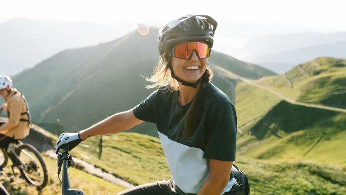 Frau mit Mountainbike und Helm auf Bergpfad bei sonnigem Wetter