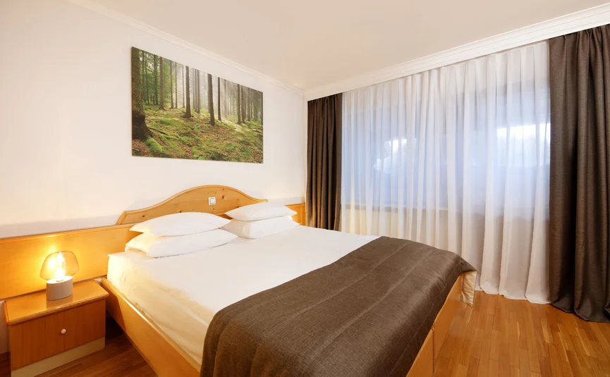 Gezellige slaapkamer met groot bed, nachtkastje en bos schilderij