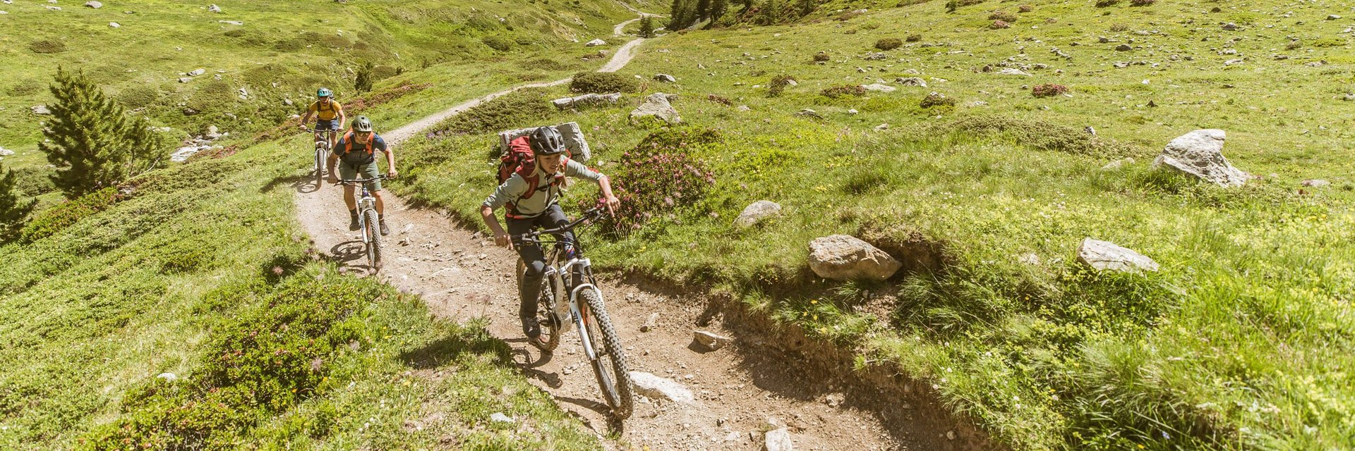 Three mountain bikers riding on narrow trail in green mountainous landscape