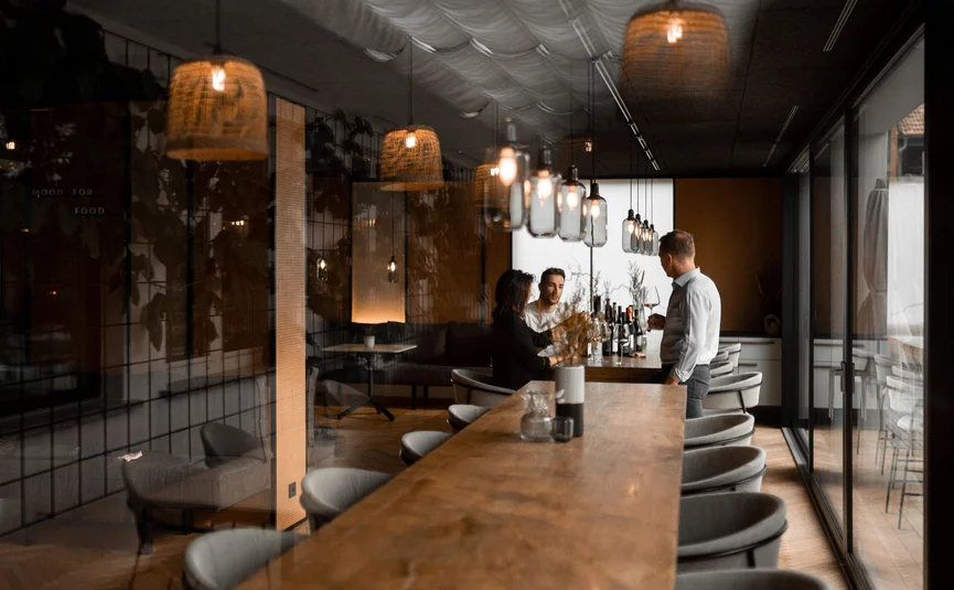 Three people drinking wine at a long wooden table in a modern room