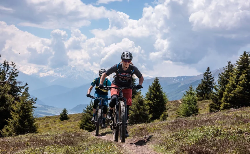 Zwei Mountainbiker fahren einen Bergpfad mit Bergblick hinauf
