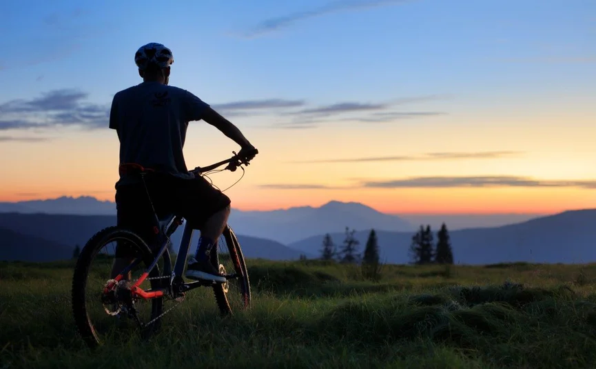 Fietser kijkt bij zonsondergang naar bergen en grasland