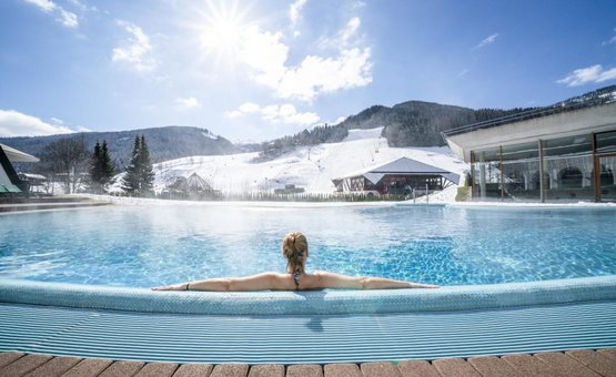 Short getaway with ski or therme Person relaxing in heated outdoor pool with snow-covered mountains in background