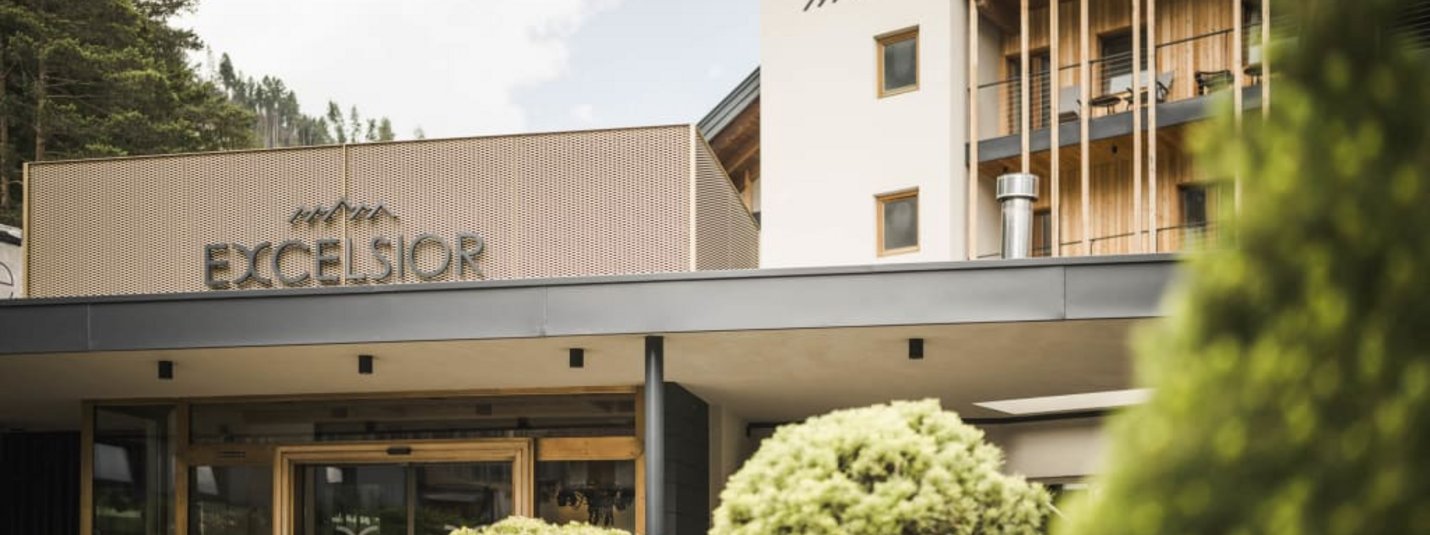 Entrance and facade of Excelsior hotel with green trees and mountains behind