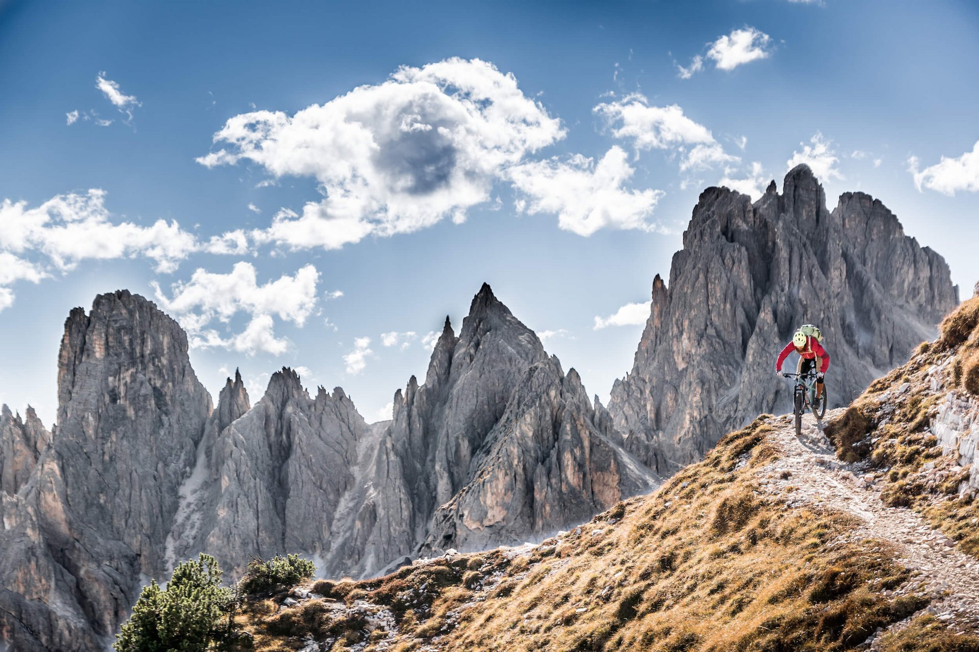 Mountainbiker fährt auf schmalem Pfad in den Bergen unter blauem Himmel