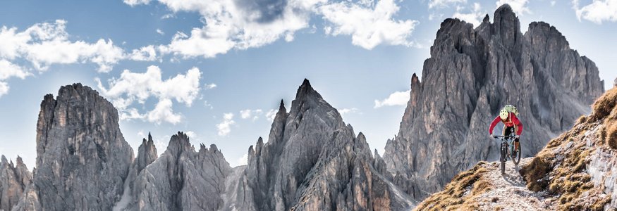 Mountain biker riding on narrow trail in mountains under blue sky