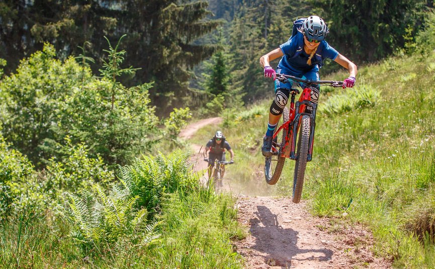 Mountainbiker springt auf einem Waldweg mit einem zweiten Radfahrer im Hintergrund