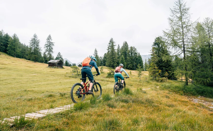Twee mountainbikers fietsen op een bospaadje in een groen berglandschap
