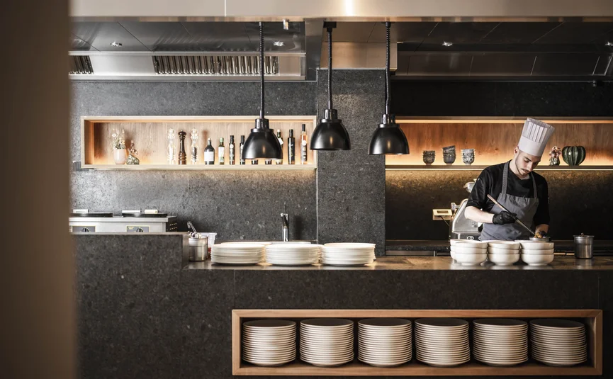 Chef in modern kitchen with hanging lights and stacked plates