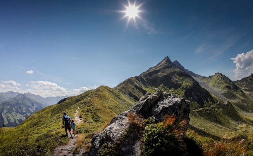 Activity holidays Hikers walking on a mountain trail under a bright sun in the Alps