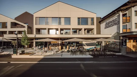 Was steckt hinter dem Umweltengagement von Bikehotels? Modernes Gebäude mit Außenterrasse und Sitzplätzen bei Sonnenschein