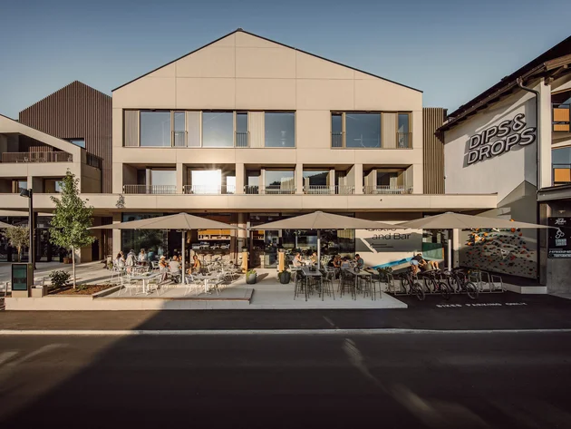 Was steckt hinter dem Umweltengagement von Bikehotels? Modernes Gebäude mit Außenterrasse und Sitzplätzen bei Sonnenschein