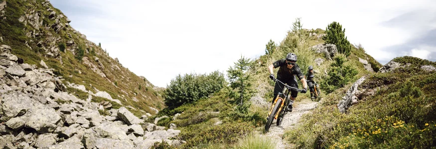 Bruneck - Kronplatz © Martina Wunderle - Flo Distl Zwei Mountainbiker fahren auf einem engen Bergpfad durch felsiges Gelände