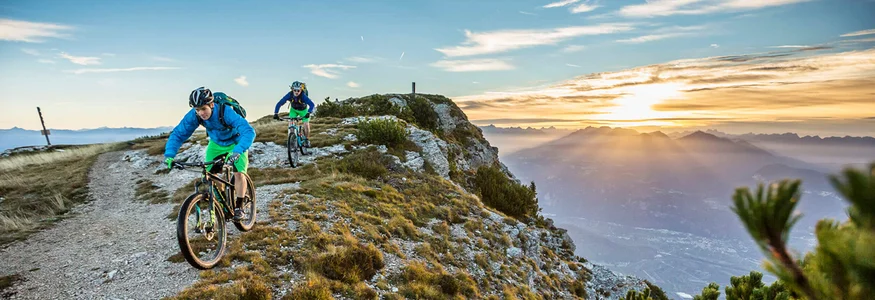 Zwei Mountainbiker fahren auf einem Bergpfad bei Sonnenuntergang