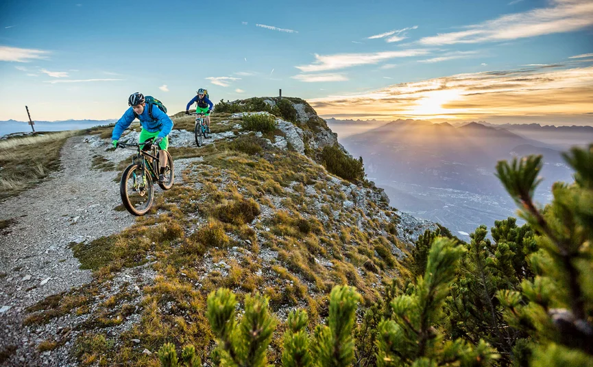 Zwei Mountainbiker fahren auf einem Bergpfad bei Sonnenuntergang