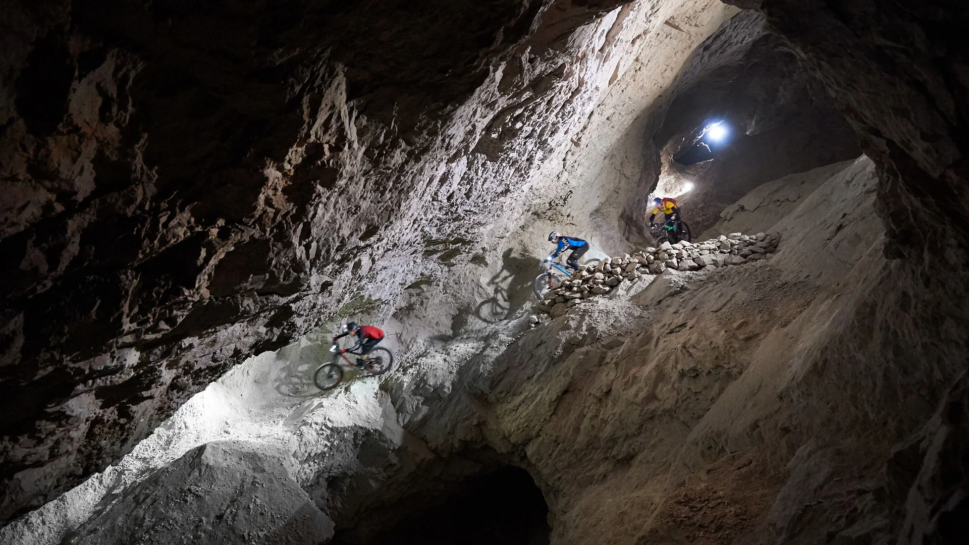 Drei Mountainbiker fahren in einem beleuchteten Bergwerkstunnel