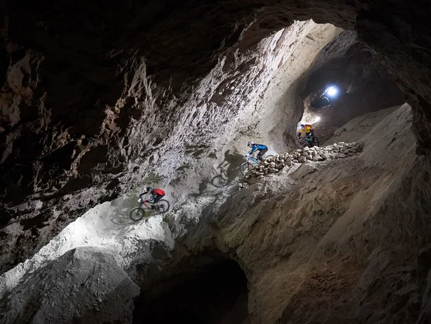 Drei Mountainbiker fahren in einem beleuchteten Bergwerkstunnel