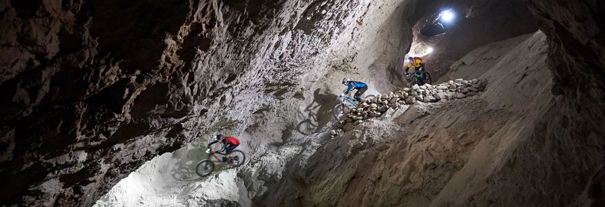 Drei Mountainbiker fahren in einem beleuchteten Bergwerkstunnel