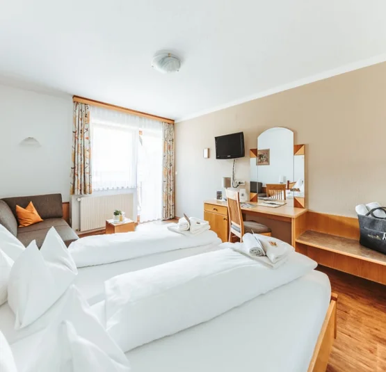 Helles Hotelzimmer mit zwei Einzelbetten, Sofa, Schreibtisch und TV