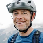 Mann mit Fahrradhelm und Rucksack vor Bergpanorama