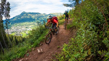 Zwei Mountainbiker fahren auf einem schmalen Bergpfad mit Blick auf ein Tal