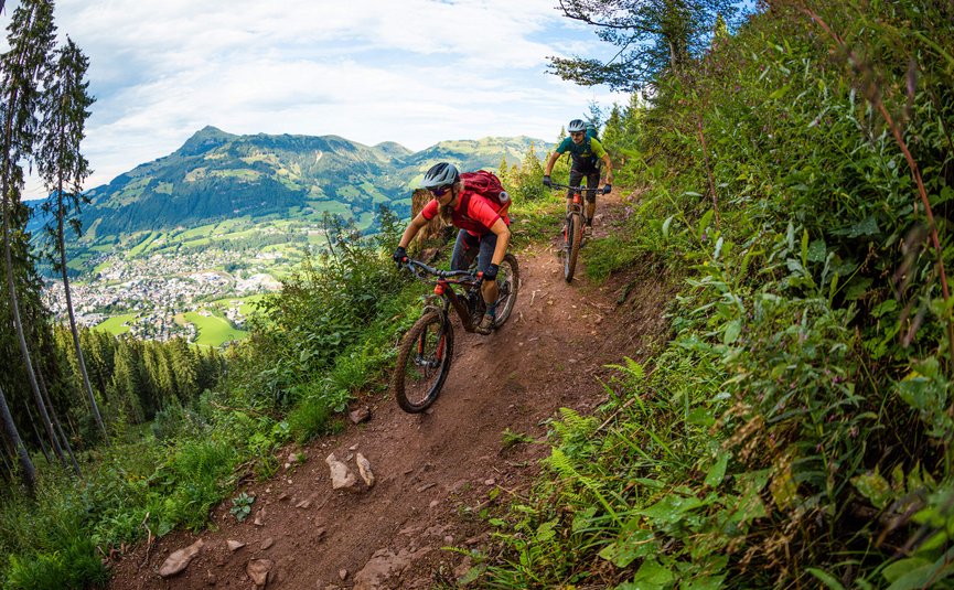 Hahnenkamm Trail © TVB Kitzbüheler Alpen-Brixental, Fotograf Andreas Meyer Zwei Mountainbiker fahren auf einem schmalen Bergpfad mit Blick auf ein Tal