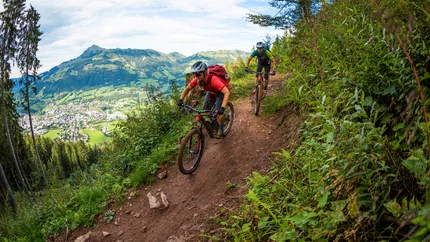 Zwei Mountainbiker fahren auf einem schmalen Bergpfad mit Blick auf ein Tal