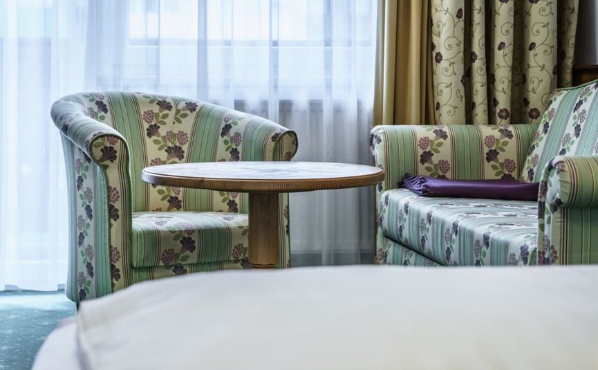 Bike week Two patterned armchairs and a round wooden table near a window with curtains