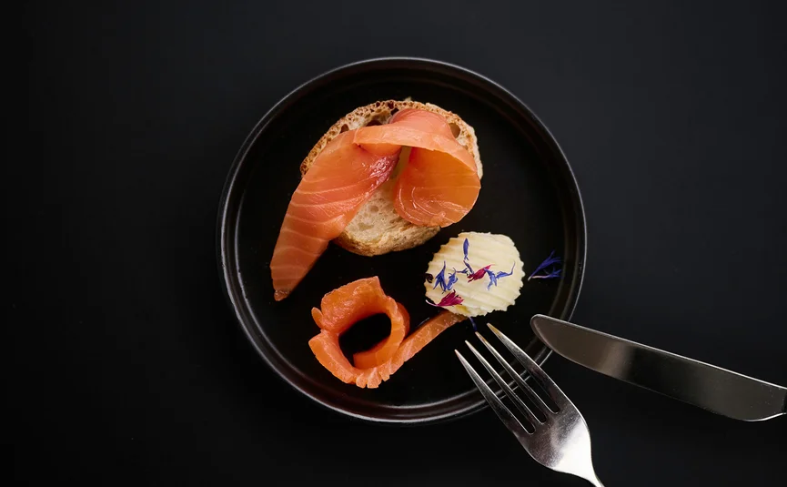HIRBEN Naturlaub **** © David Rasche Smoked salmon on bread with butter and edible flowers on black plate
