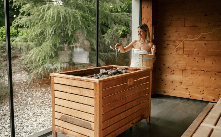 Puradies © Jeppe Zoffmann Frau gießt Wasser auf Steine in Sauna mit Fenster zum Garten