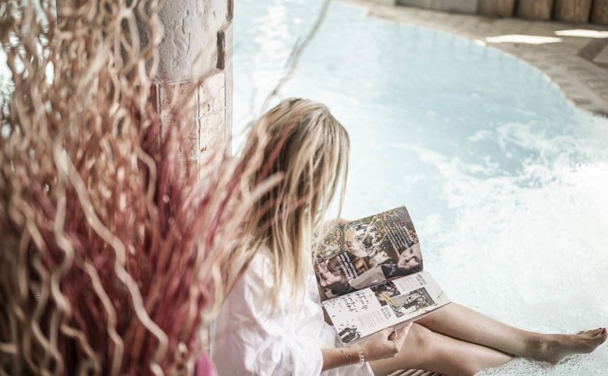 Vrouw ontspant met een boek bij de rand van een binnenzwembad