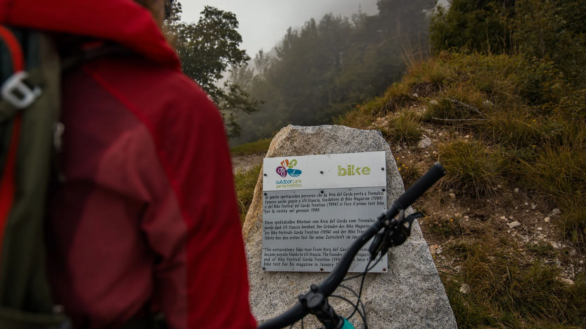 Persoon bij steen met fietsparkinformatie in mistig bos