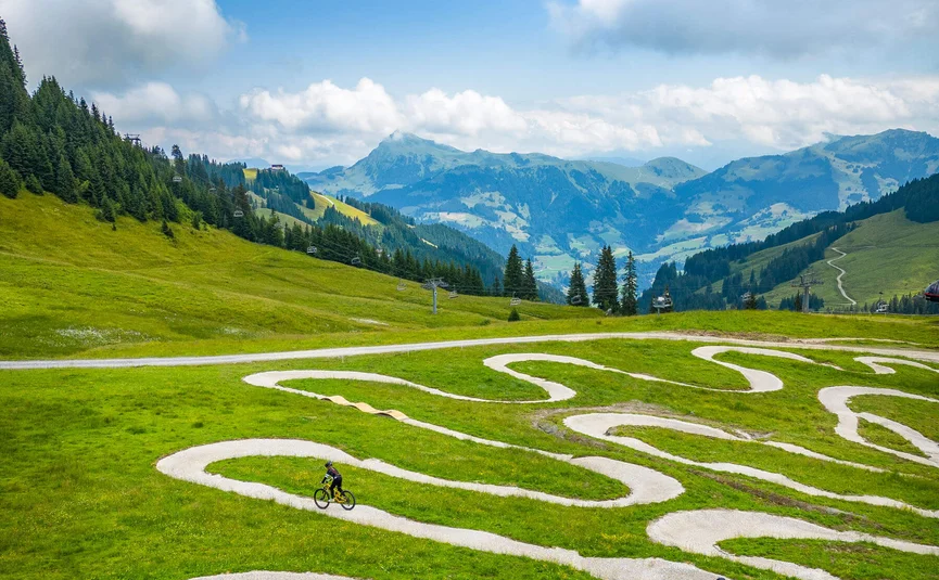 Drei Mountainbiker auf einem verschlungenen Weg in grünen Bergen bei bewölktem Himmel