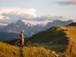 Mountainbiker steht auf Bergpfad mit Blick auf Dolomiten bei Sonnenuntergang