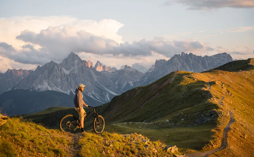 Mountainbike-Urlaub in der Region 3 Zinnen Dolomites © Elias Ochner - Stefan Schwabl Mountainbiker steht auf Bergpfad mit Blick auf Dolomiten bei Sonnenuntergang
