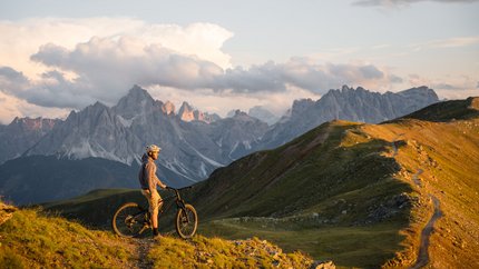 Mountainbiker steht auf Bergpfad mit Blick auf Dolomiten bei Sonnenuntergang