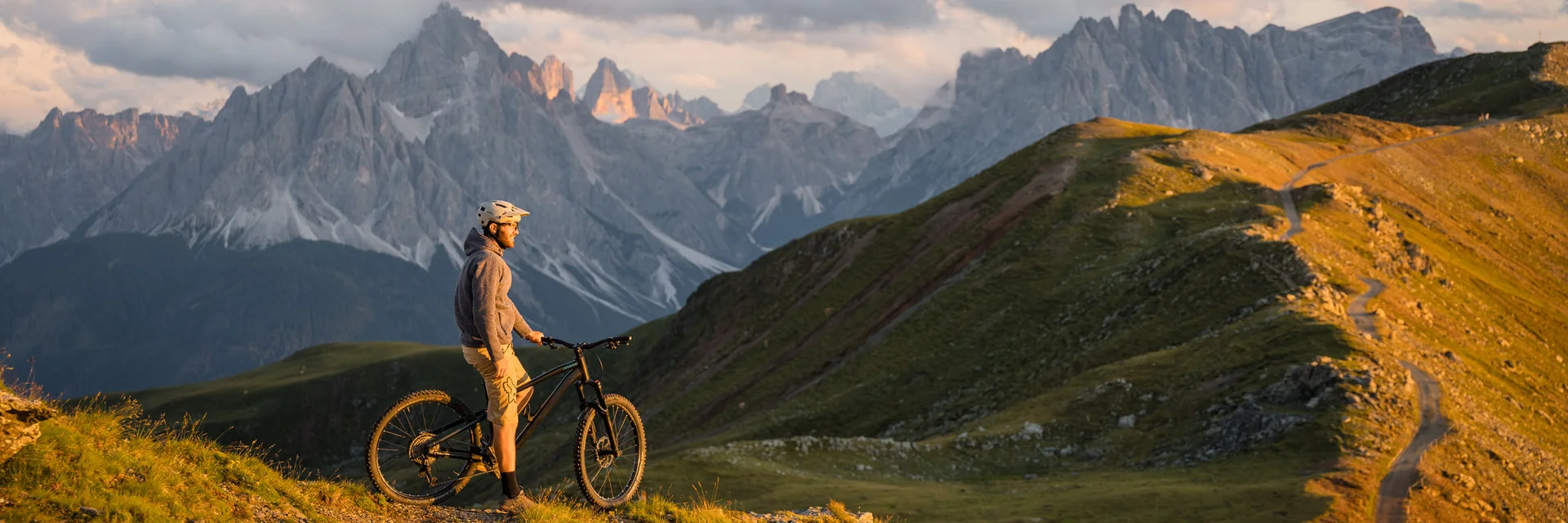 Mountainbiker steht auf Bergpfad mit Blick auf Dolomiten bei Sonnenuntergang