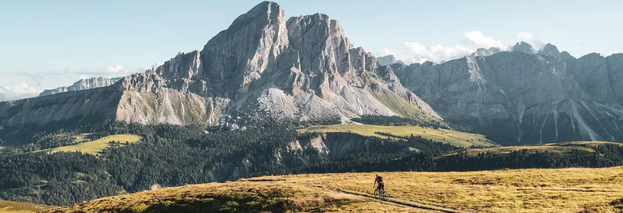 Cyclist on trail overlooking large mountain range under clear sky